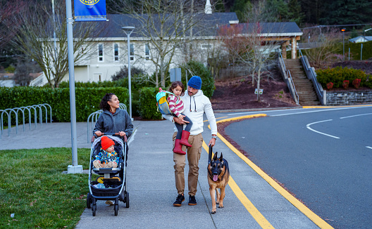 A preschool age Eurasian girl walks with her mom and dad, pet dog, and younger brother to school on a cool autumn morning in Oregon.