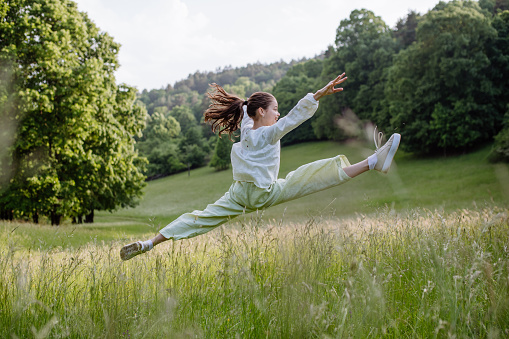 Portrait of beautiful young girl jumping in tall grass, having fun, enjoying warm spring day.