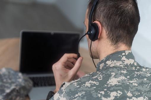 Young hispanic man army soldier using laptop sitting on table at home. High quality photo