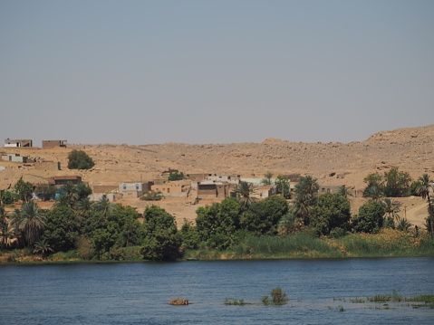 A body of water stretches out in the foreground, with a small village visible in the background. The village is made up of several buildings nestled along the Nile River, creating a picturesque scene.