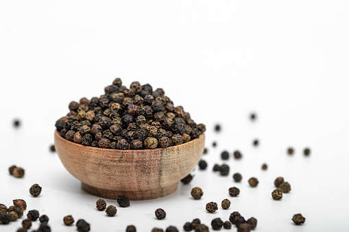 Black pepper whole grain in a wooden bowl and scattered around it
