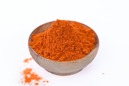 Sweet paprika powder in a wooden bowl on a white background, intensely orange
