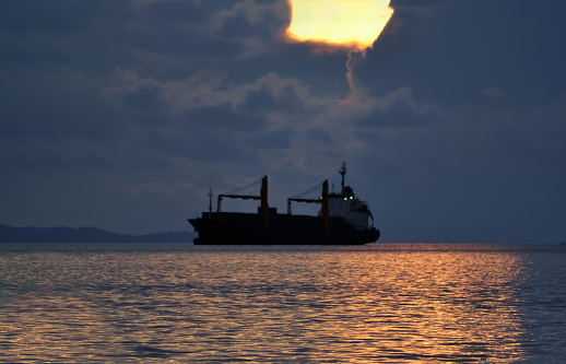 The beautiful image of a colossal cargo vessel gently mooring at sea beneath the captivating expanse of a dramatic sky.
