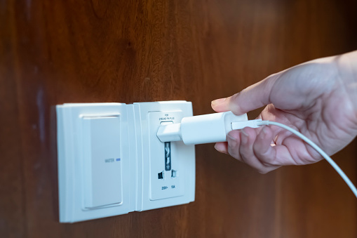 Plugging USB cable to two round pin plug power adapter. Woman hold USB plug against wall charger. Plug-in connector into wall wooden outlet or socket with AC adapter.