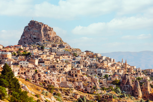 This stunning aerial shot captures the picturesque town of Uchisar in Cappadocia, Turkey, on a bright sunny day. The unique landscape features houses carved into the rocky terrain, blending seamlessly with the natural rock formations. In the distance, the iconic Uchisar Castle overlooks the scenic Pigeon Valley, adding to the charm of this historic town. The image offers a captivating glimpse into the fascinating architecture and natural beauty of Cappadocia.