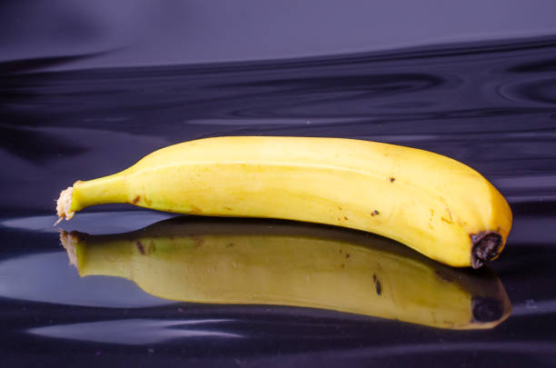 A white plate on a white background with fruit consisting of a yellow and green banana and red apple on the plate