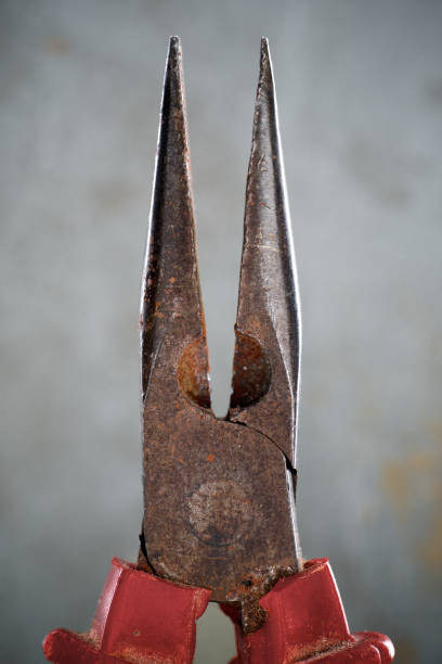 Close up of slim metal pliers on a gray background