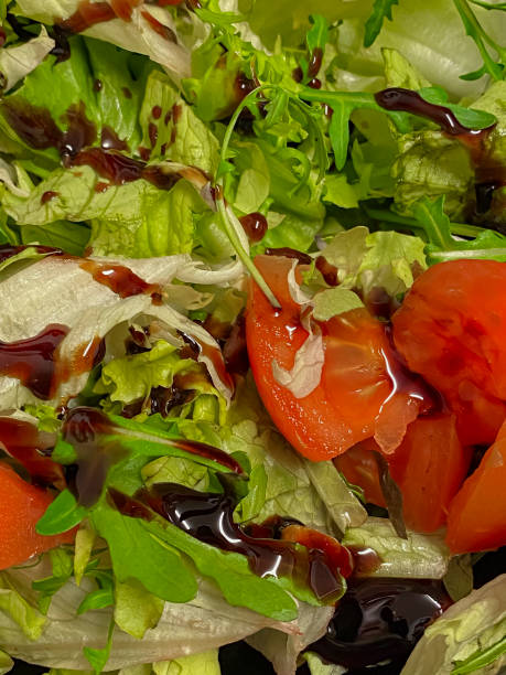 A vibrant dish of green salad served in a sleek white plate. The salad is composed of fresh spinach and onion, mixed with a medley of colorful cherry tomatoes.