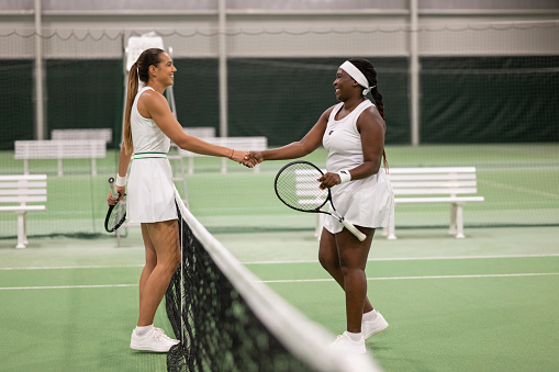 Multiracial female tennis players shaking hands after friendly match. Sport and healthy lifestyle concept.