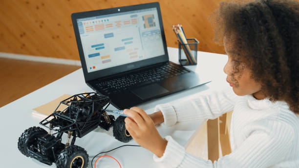 istock African girl build robotic car while using wires while using laptop. Erudition. 2052748283