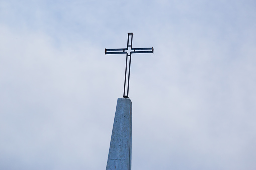 Wooden cross on a simple steeple set against a sunny summer blue sky.