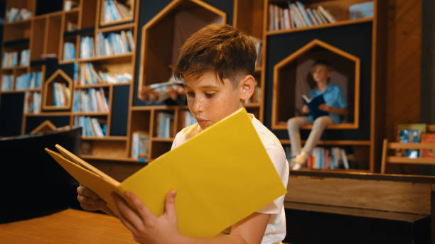 istock Boy reading a book while group of smart students sitting at library. Erudition. 2052796009
