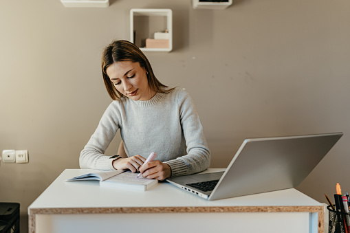 A woman harmonizes her digital presence with a literary pause, choosing to read a book in front of her laptop, a practice that underscores the balance between staying informed online and the reflective pause offered by traditional reading