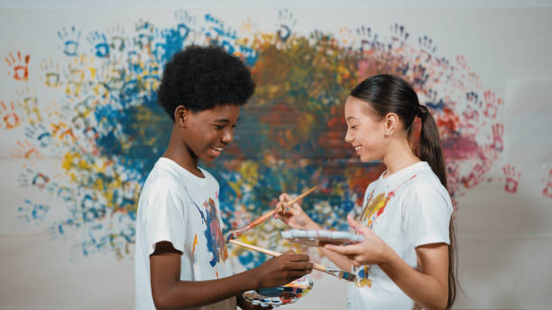 istock Smiling diverse children paint color on each other shirt at wall. Edification. 2052824387
