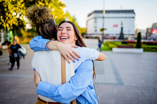 Two young cheerful female friends hugging in the city