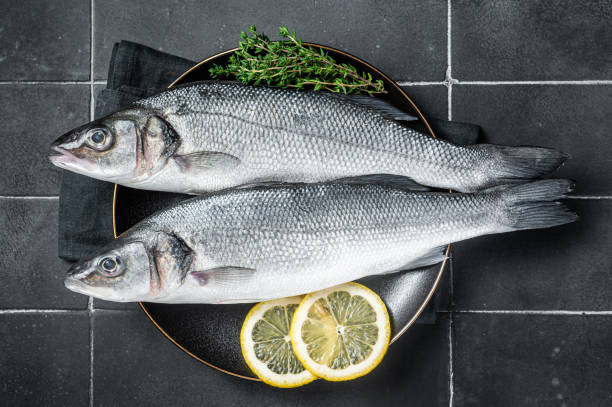 istock Fresh Raw Sea Bass fish with lemon and thyme. Black background. Top view 2052904406