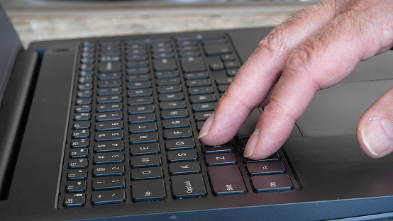 A close-up view of a senior mans hands as he types on a laptop located on a kitchen countertop. Natural light fills the room, highlighting the daily life and technology use by the elderly.