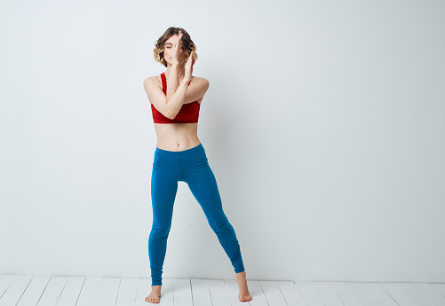 A woman in blue leggings does exercises on a light background of yoga asana. High quality photo