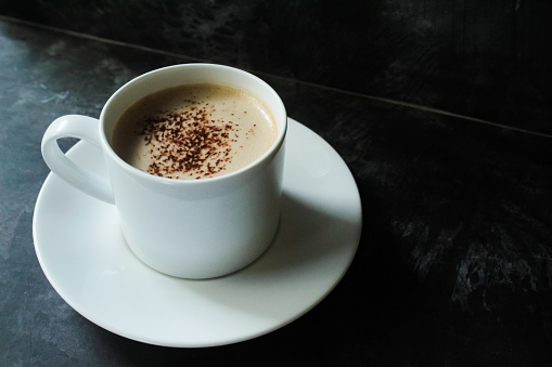 a cup of hot cappuccino coffee with cream, on a black table