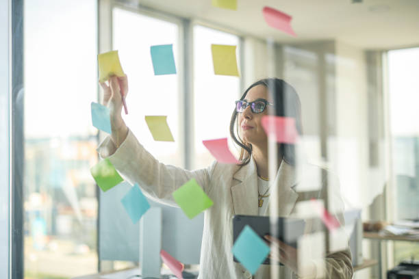 istock Businesswoman Working in Office Using Digital Tablet, Post-its and Sticky Notes Pasted on the Window 2052942527