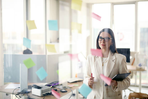 istock Businesswoman Working in Office Using Digital Tablet, Post-its and Sticky Notes Pasted on the Window 2052943064