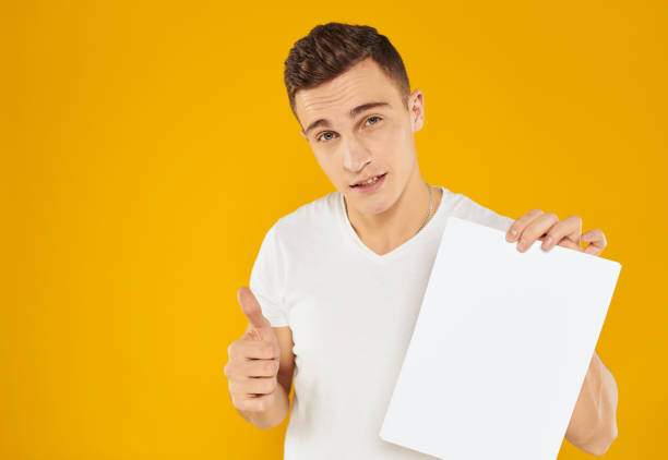 istock Guy with white sheet of paper mockup yellow background Copy Space 2053002082