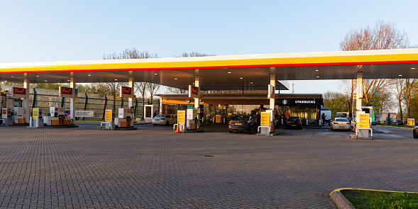 Netherlands, South Holland, Reeuwijk, April 19th 2023, small group of people refueling their cars at the Shell gas station 'De Andel' at the A12 highway near Gouda and Reeuwijk at sunset, the A-12 is a 137 kilometer long highway crossing the country from The Hague in the East to Germany in the West