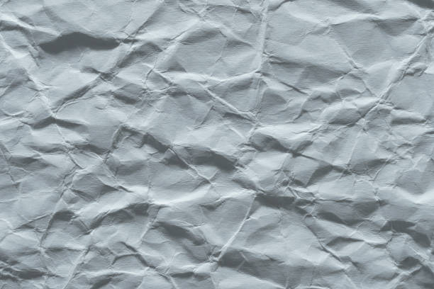 Full frame of crumpled white paper texture, highlighting the shadows and depth created by the folds.