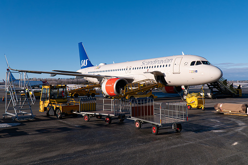 Umeå, Sweden - February 27th 2024: A SAS (scandinavian airline) airplane, Airbus A320 neo, at Umeå Airport, with ground handling operations ongoing. Winter conditions, blue sky, frost