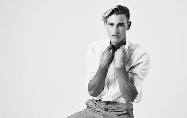 A guy of model appearance in black clothes poses on a black studio background. Male fashion portrait