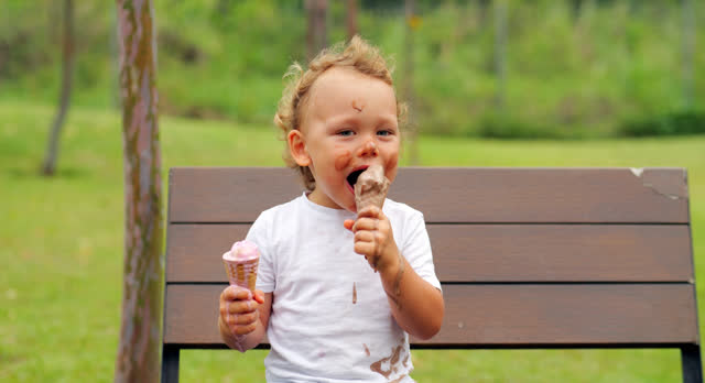 Young boy with two melting ice cream cones in stained t-shirt has fun in park