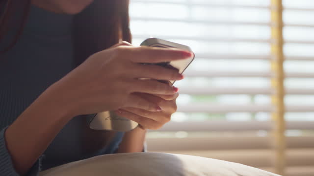 Close-up of young women hand  Hand of woman using smartphone social media internet surfing near window in the living room at home, typing message online pleasure lifestyle