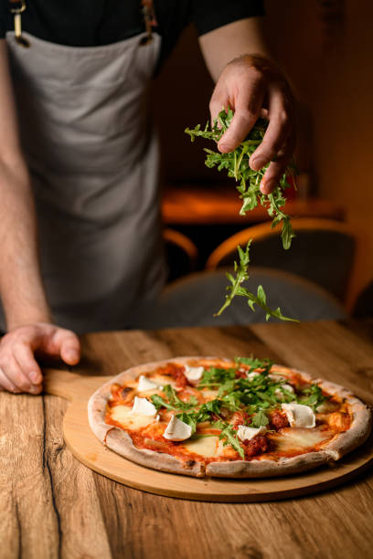 istock Fresh arugula on pizza. Chef culinary artistry at work 2053145699