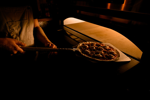 With precision, the chef slides the pizza into the oven using an oven shovel, commencing the baking process.