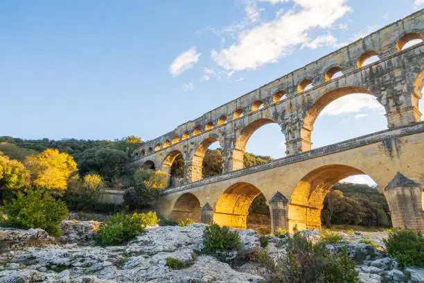 Famous Pont du Gard at setting sun. Ancient Roman three-tiered aqueduct bridge. Built in the 1st century AD to carry water to the Roman colony of Nemausus (Nîmes).  Photography taken in Vers-Pont-du-Gard, Provence, southern France.