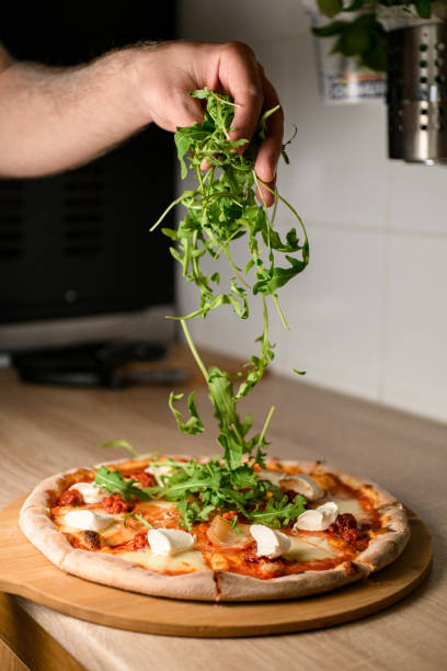The chef adds a finishing touch by gently scattering arugula over the completed pizza, elevating its presentation and taste.