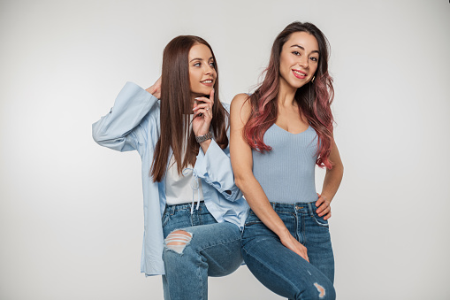 Two beautiful young women models with smiles in fashionable denim clothes posing and having fun on a white background. Pretty girlfriends