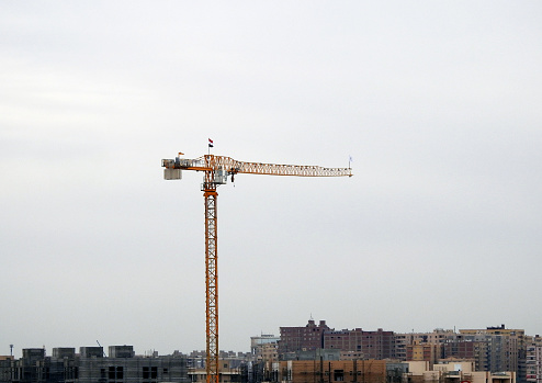 Cairo, Egypt, February 23 2024: A crane tower with the Egyptian flag waving on it, A construction site of new residential buildings and high rise with cranes to transport heaving objects, selective focus