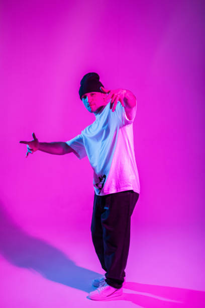 istock Cool stylish b-boy dancer guy in trendy clothes with a hat posing and dancing in a creative studio with pink and neon lights 2053209607