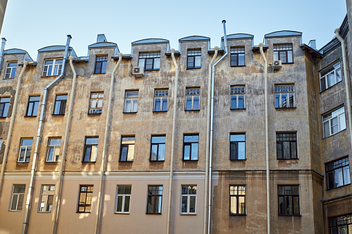 View from below of old courtyard yellow wall in St. Petersburg, Russia. Wall, windows, tubes and part of blue sky