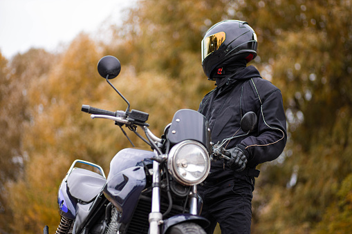 Motorcycle safety helmet concept. Unrecognizable biker holding helmet next to motorbike near the road. Motorcyclist holding safety helmet next to his motorbike near the road