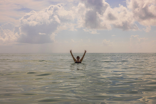 Scene capturing a woman with her hands raised in the water against a backdrop of a pale blue sky. Miami Beach. USA.