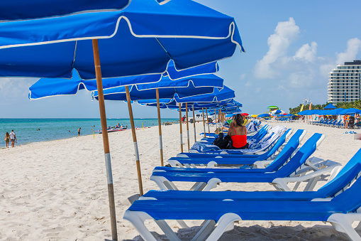 Miami Beach. USA. 03.03.2024. Beautiful view of Miami's sandy beach with blue sunbeds and umbrellas, where people relax beneath the umbrellas on loungers.