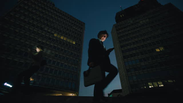 SLO MO Business People With Smart Phones Walking Below Buildings In City At Night