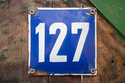 Weathered grunge square metal enameled plate of number of street address with number 127