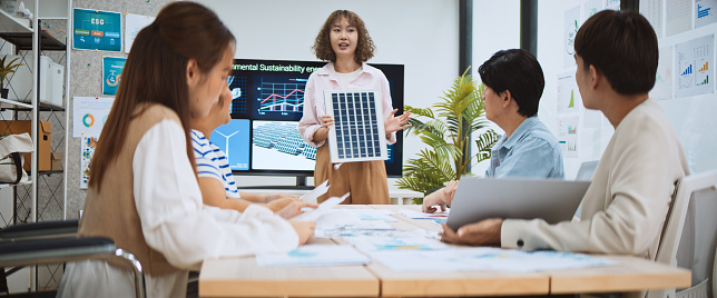 Asian business people team brainstorm meeting in sustainable corporate office. Presentation ESG project planning, solar panel, wind turbine power energy generation. Environmental conservation concept photo