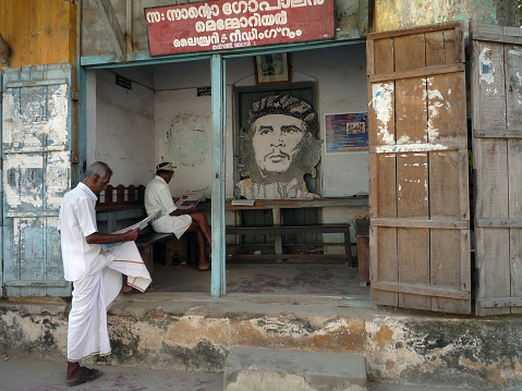 India, kerala, Cochin: Indian men read the newspaper in front of a public office of the Communist Party of Kerala with the image of Che Gevara