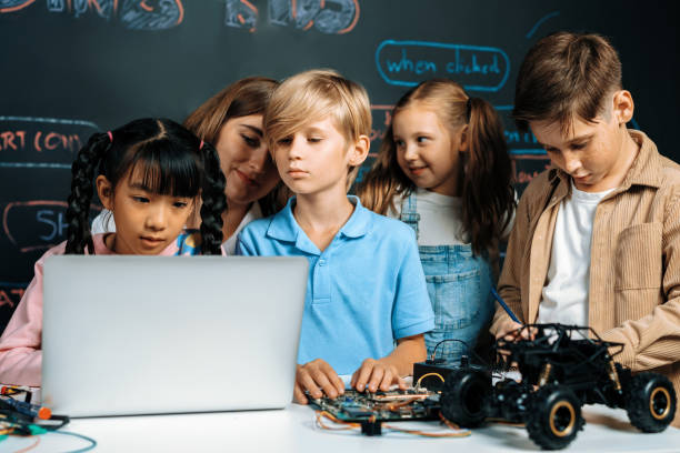 istock Girl wear pink cloth use laptop for coding while teacher watch her. Erudition. 2053382241