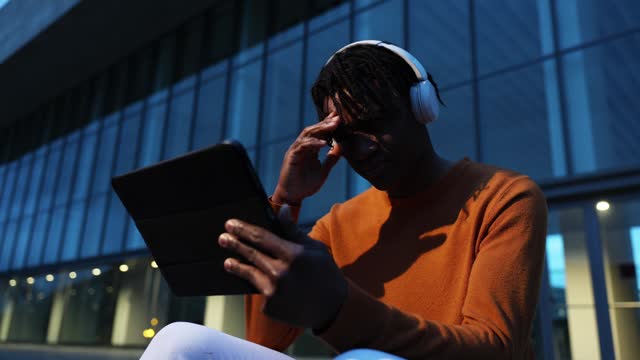 Young African American man with a tablet and headphones. The man is receiving distressing news while using the digital tablet.