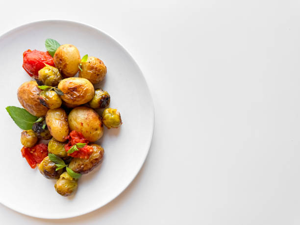 istock Roasted baby potatoes and Brussels sprouts with cherry tomatoes on white plate, garnished with basil, healthy vegetarian dish concept with space for text. 2053408540